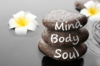 Photo of Spa stones with words Mind, Body, Soul and plumeria flowers in water, closeup. Zen lifestyle