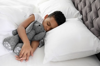 Cute little African-American boy with toy rabbit sleeping in bed