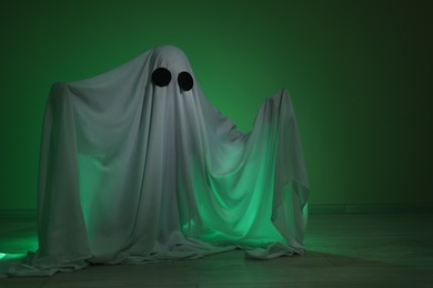 Photo of Creepy ghost. Woman covered with sheet in green light, space for text