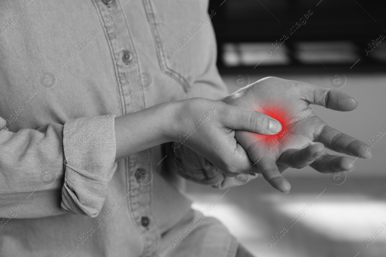 Image of Woman suffering from trigger finger indoors, closeup. Black and white photo with red accent