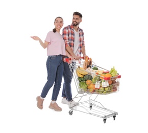 Happy couple with shopping cart full of groceries on white background