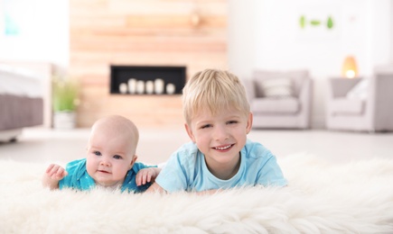 Photo of Cute boy with his little sister lying on fur rug at home