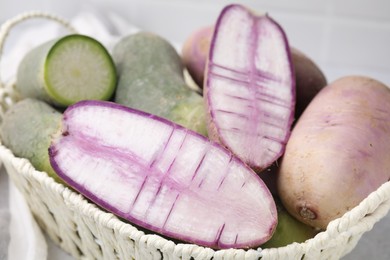 Photo of Purple and green daikon radishes in wicker basket on table, closeup