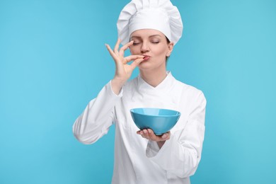 Woman chef in uniform holding bowl and showing perfect sign on light blue background