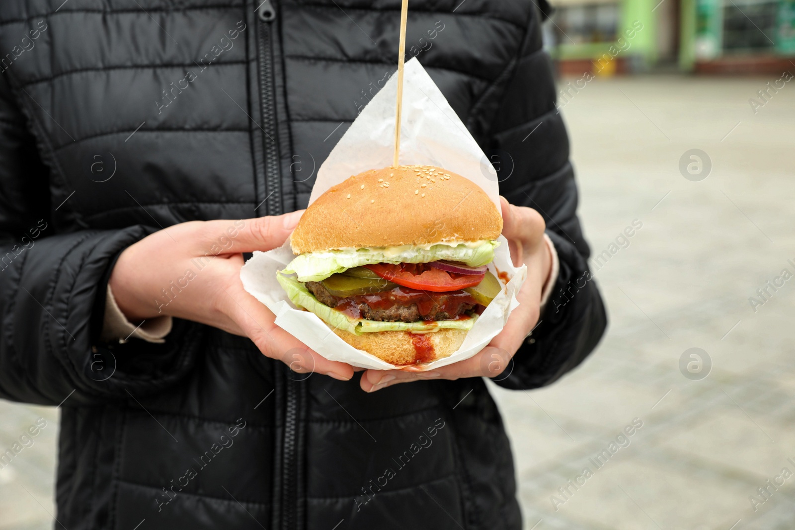 Photo of Woman holding fresh delicious burger outdoors, closeup. Street food