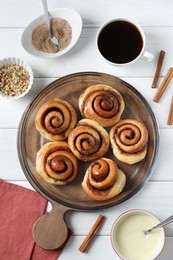 Photo of Tasty cinnamon rolls and ingredients on white wooden table, flat lay