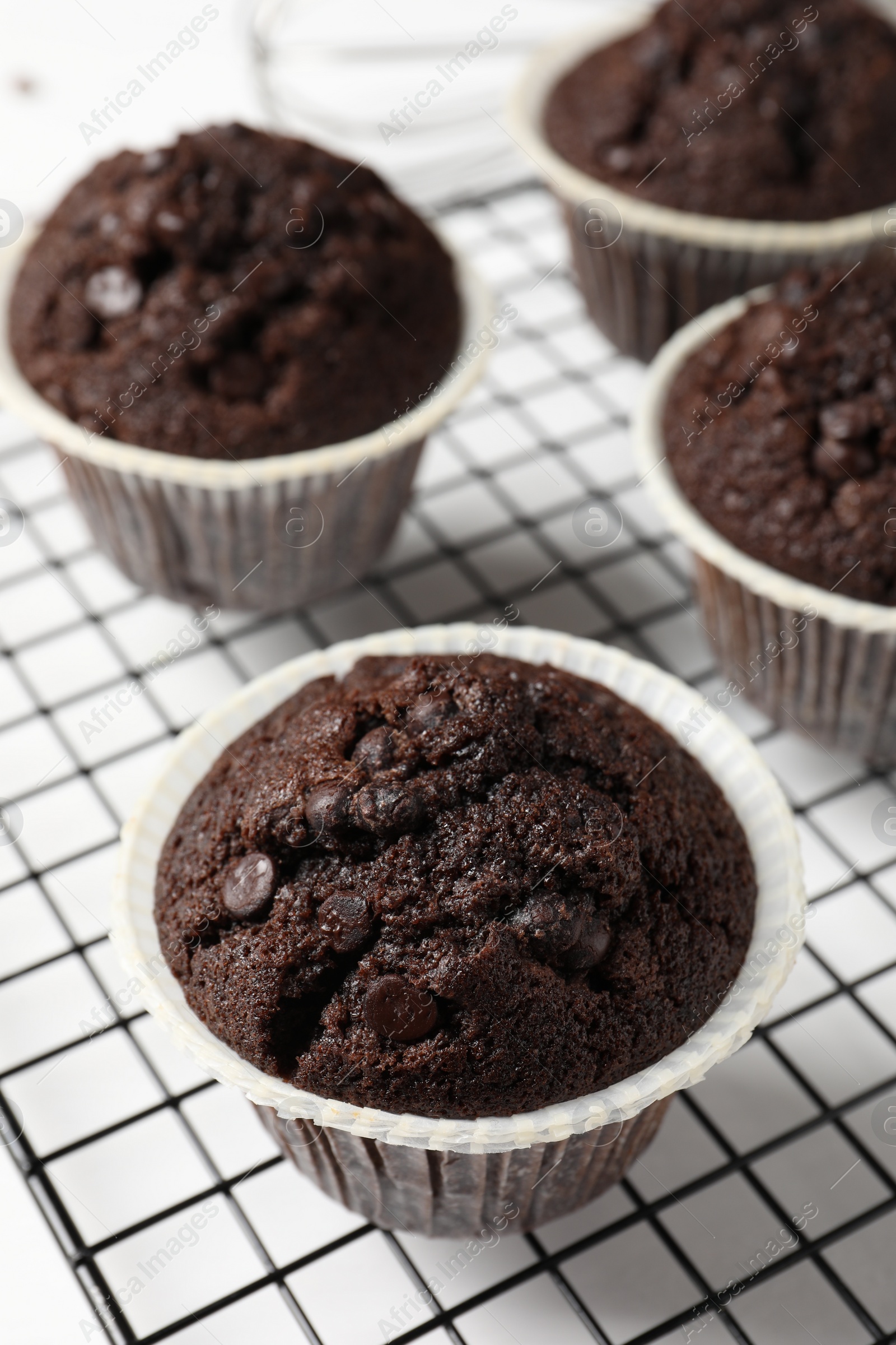 Photo of Tasty chocolate muffins and cooling rack on white table, closeup