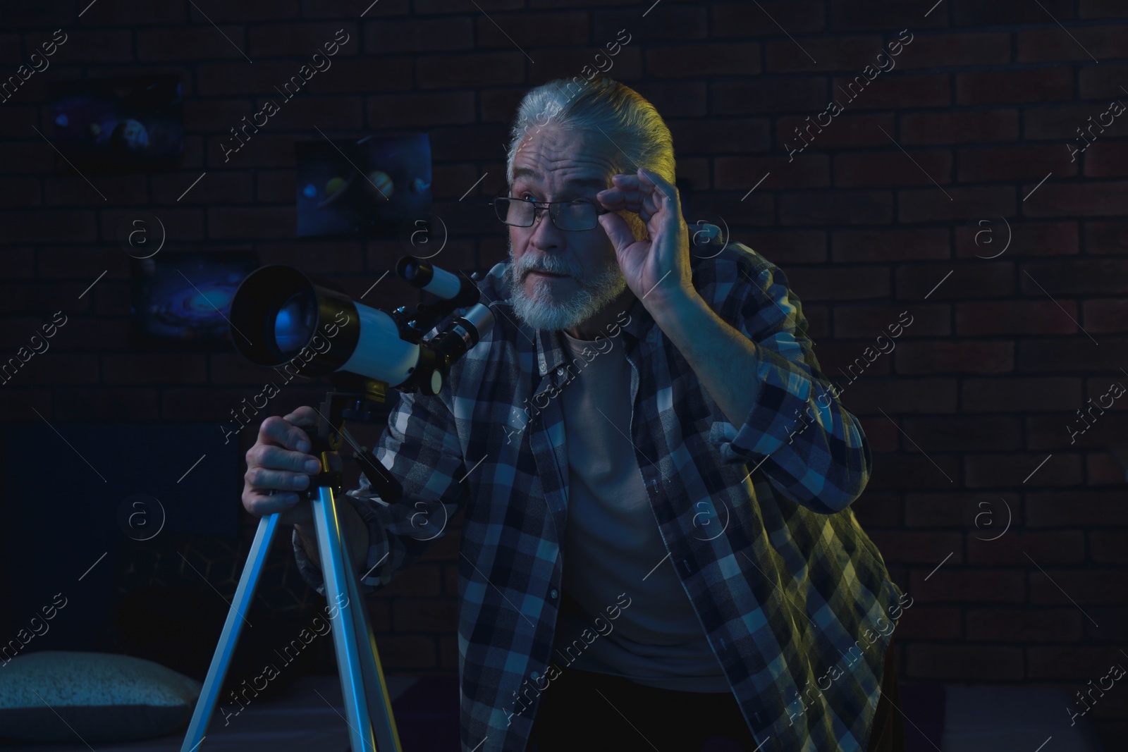 Photo of Senior man using telescope to look at stars in room