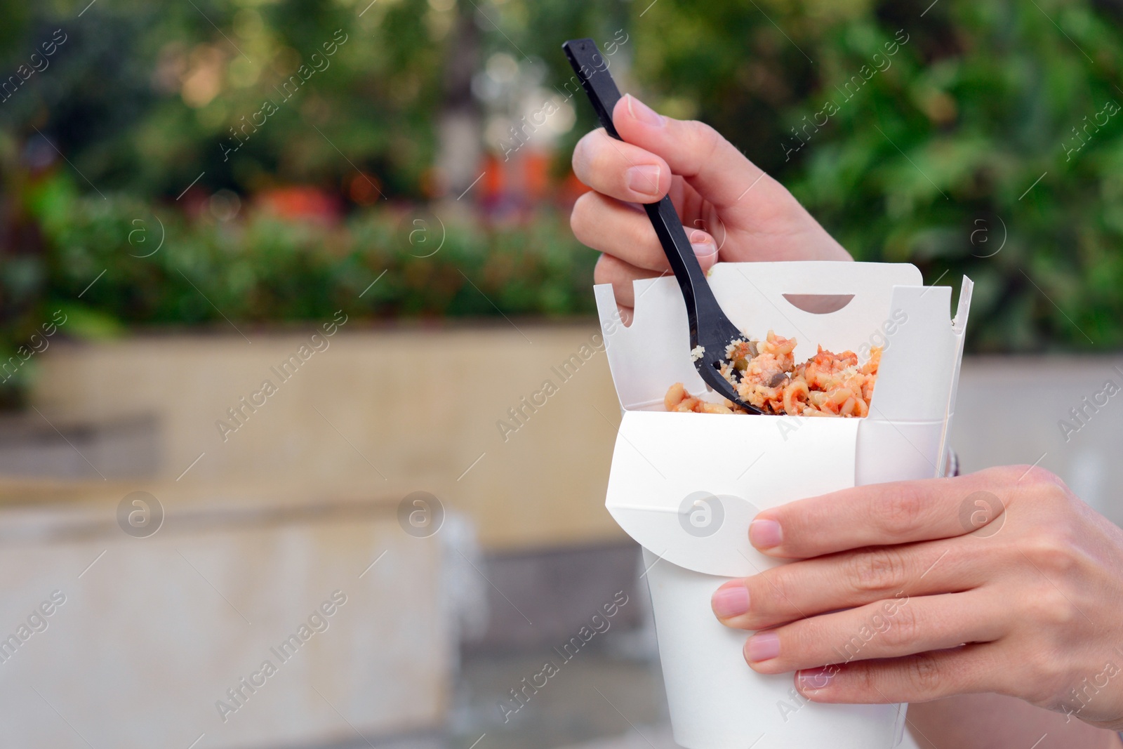 Photo of Woman eating takeaway noodles from paper box with fork outdoors, closeup and space for text. Street food