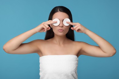 Photo of Young woman covering her eyes with cotton pads on light blue background
