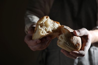 Photo of Man breaking loaf of fresh bread on dark background, closeup