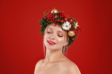 Beautiful young woman wearing Christmas wreath on red background