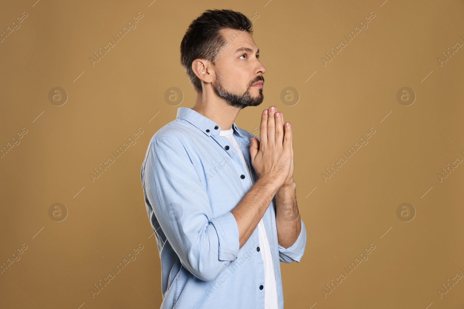 Photo of Man with clasped hands praying on beige background