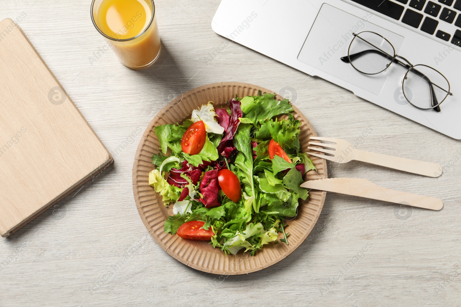 Photo of Fresh vegetable salad, glass of juice and laptop on white wooden table at workplace, flat lay. Business lunch