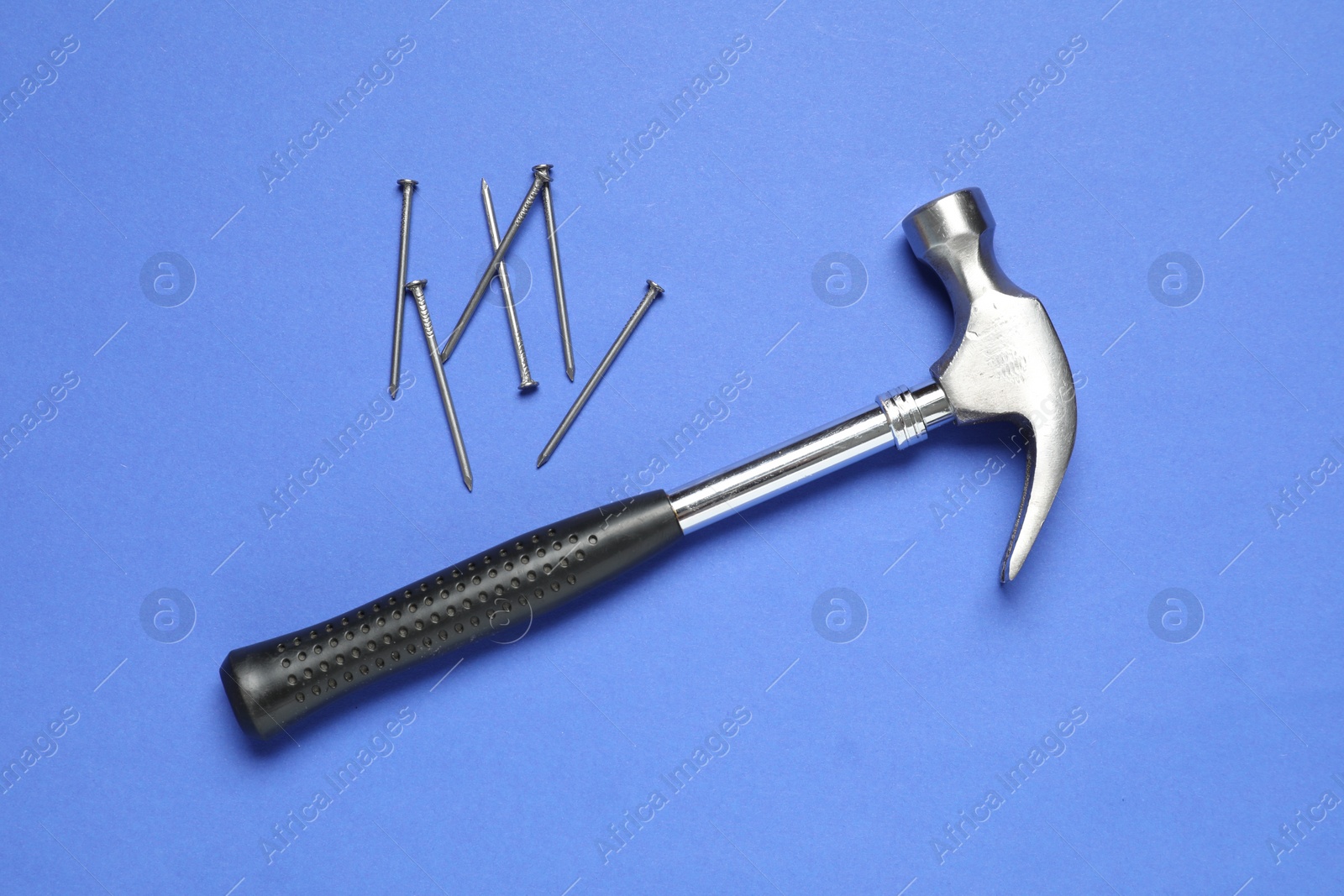 Photo of Hammer and metal nails on blue background, top view