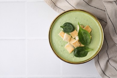 Delicious spinach cream soup with croutons in bowl on white tiled table, top view. Space for text