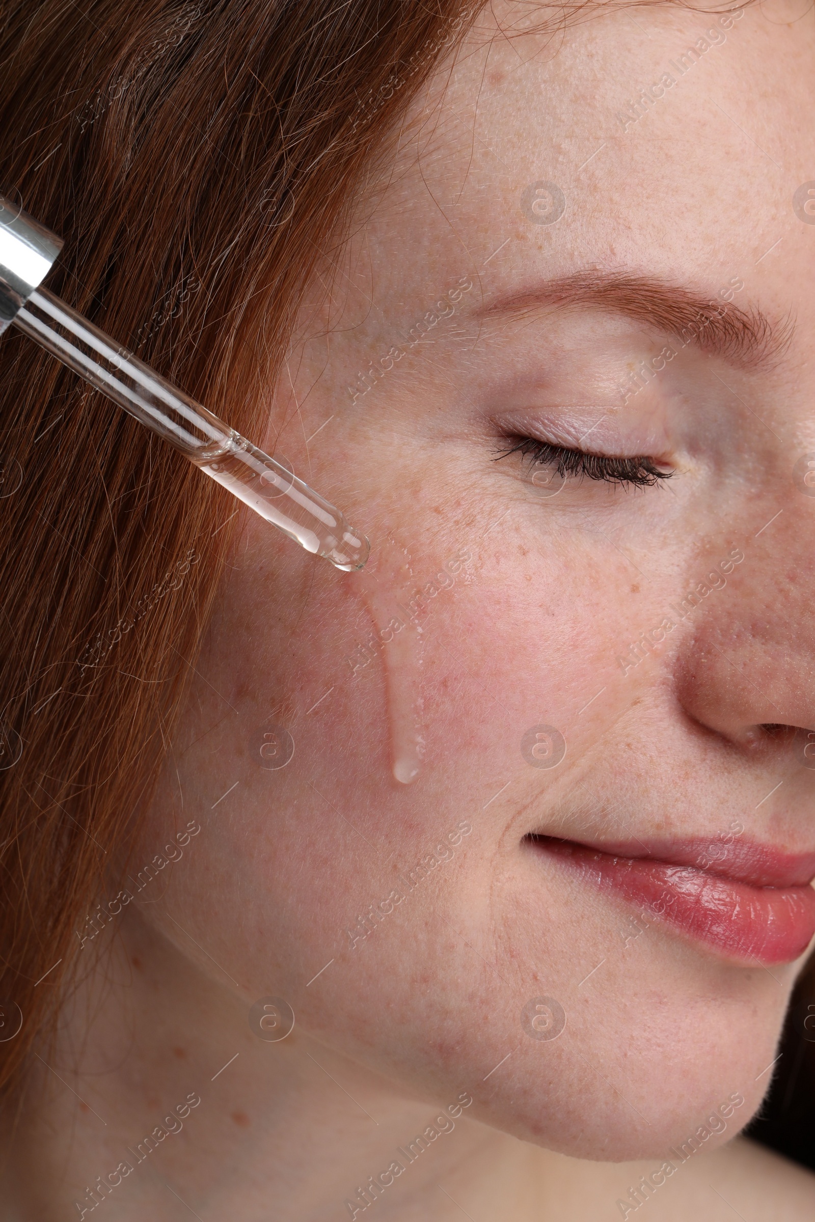 Photo of Beautiful woman with freckles applying cosmetic serum onto her face, closeup