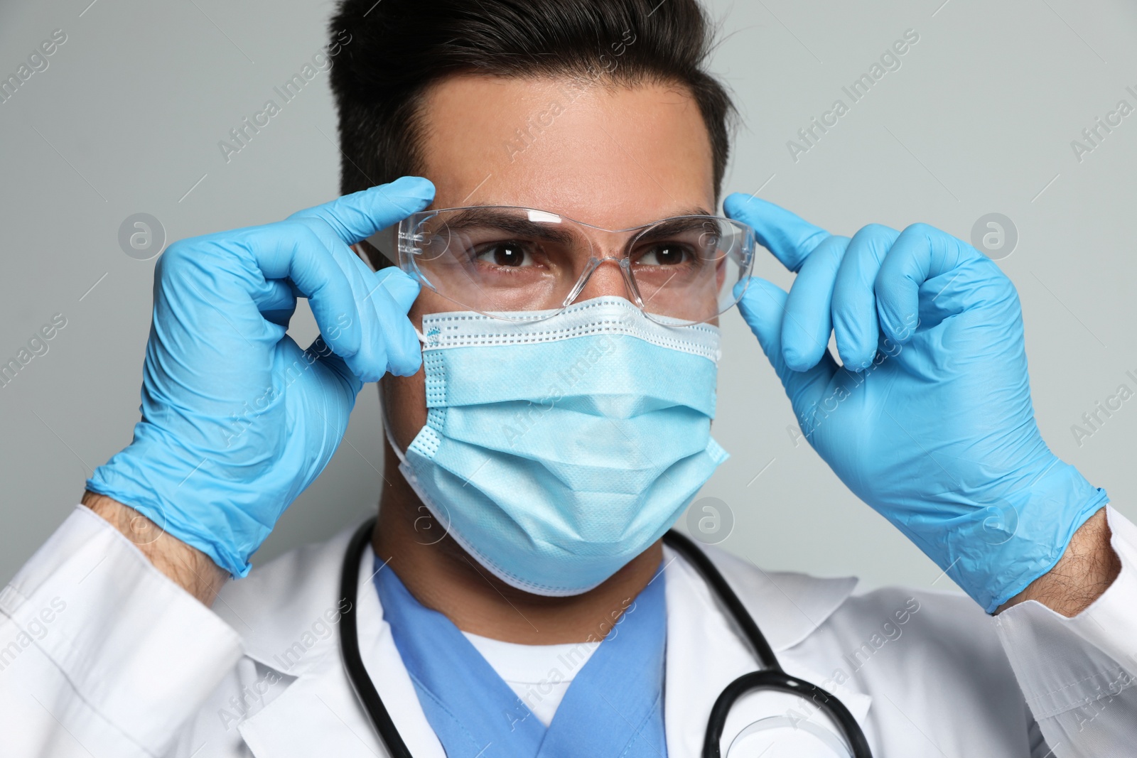 Photo of Doctor in protective mask, glasses and medical gloves against light grey background