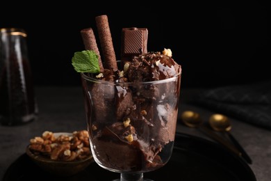 Photo of Tasty chocolate ice cream with sauce, nuts and wafer rolls in glass dessert bowl on table, closeup