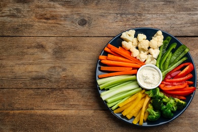 Photo of Plate with celery sticks, other vegetables and dip sauce on wooden table, top view. Space for text