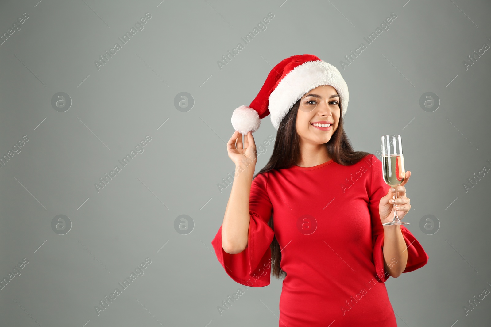 Photo of Young beautiful woman in Santa hat with glass of champagne on grey background. Christmas celebration