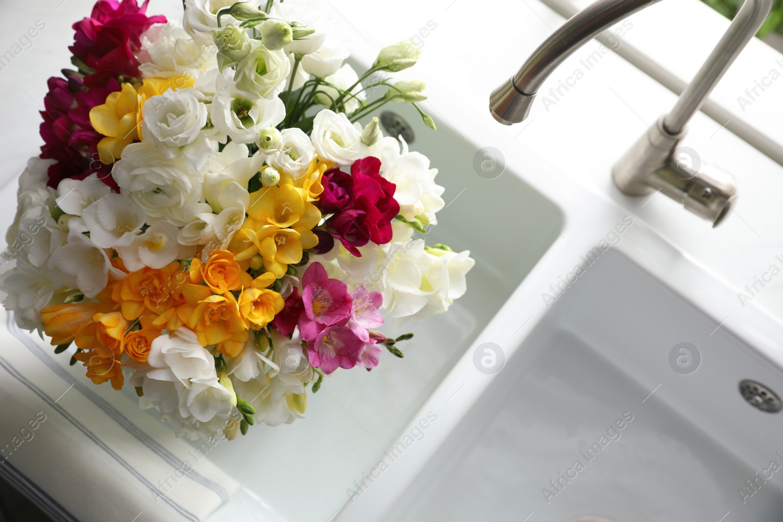 Photo of Beautiful bouquet with fresh freesia flowers in kitchen sink, above view