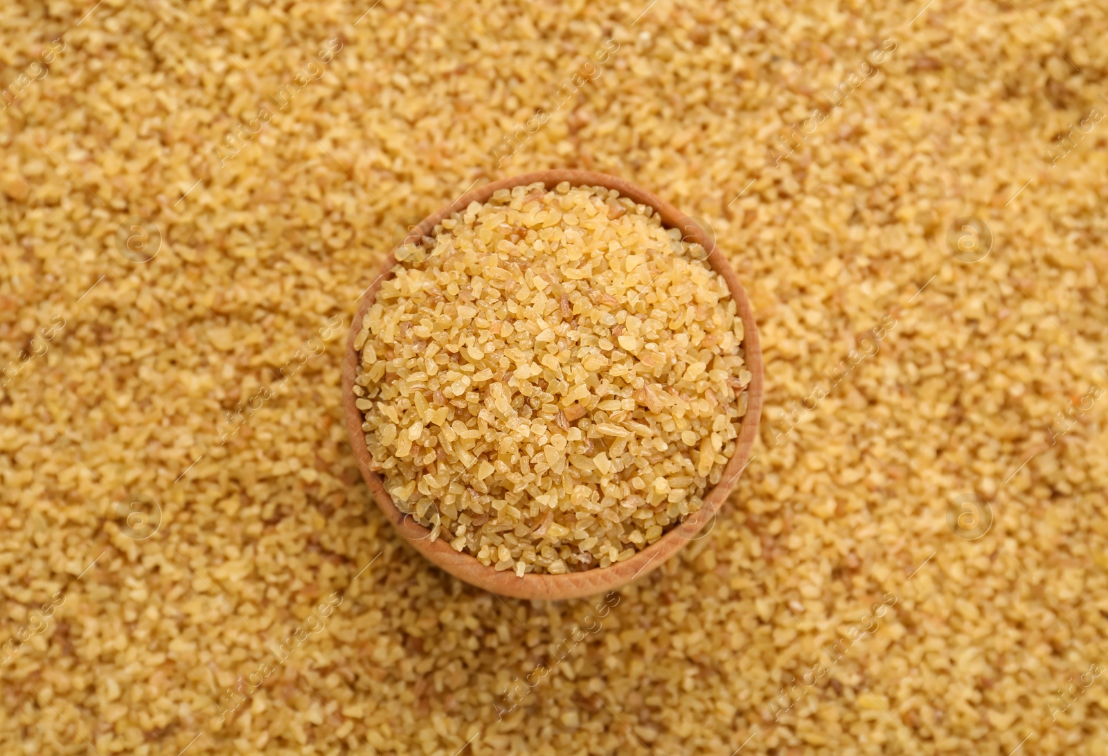 Photo of Wooden bowl on pile of uncooked bulgur, top view