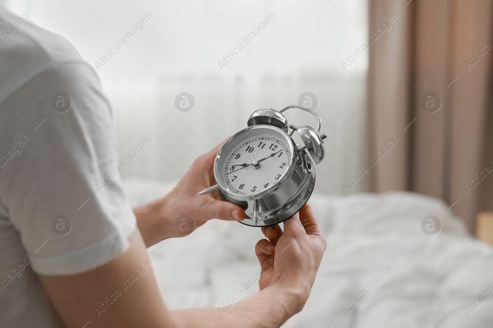 Photo of Man with alarm clock in bedroom, closeup of hands