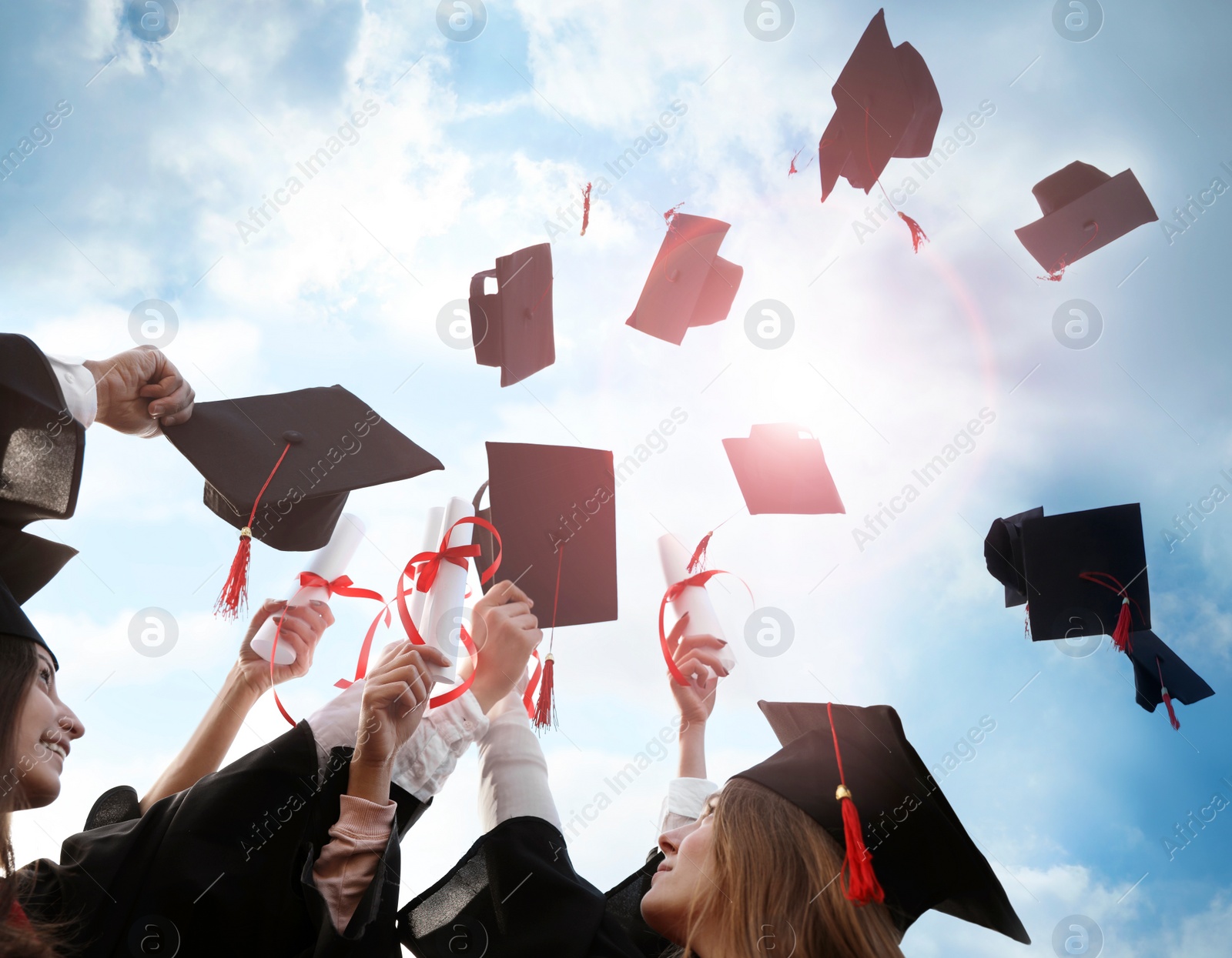 Image of Happy students with diplomas throwing graduation hats in air outdoors