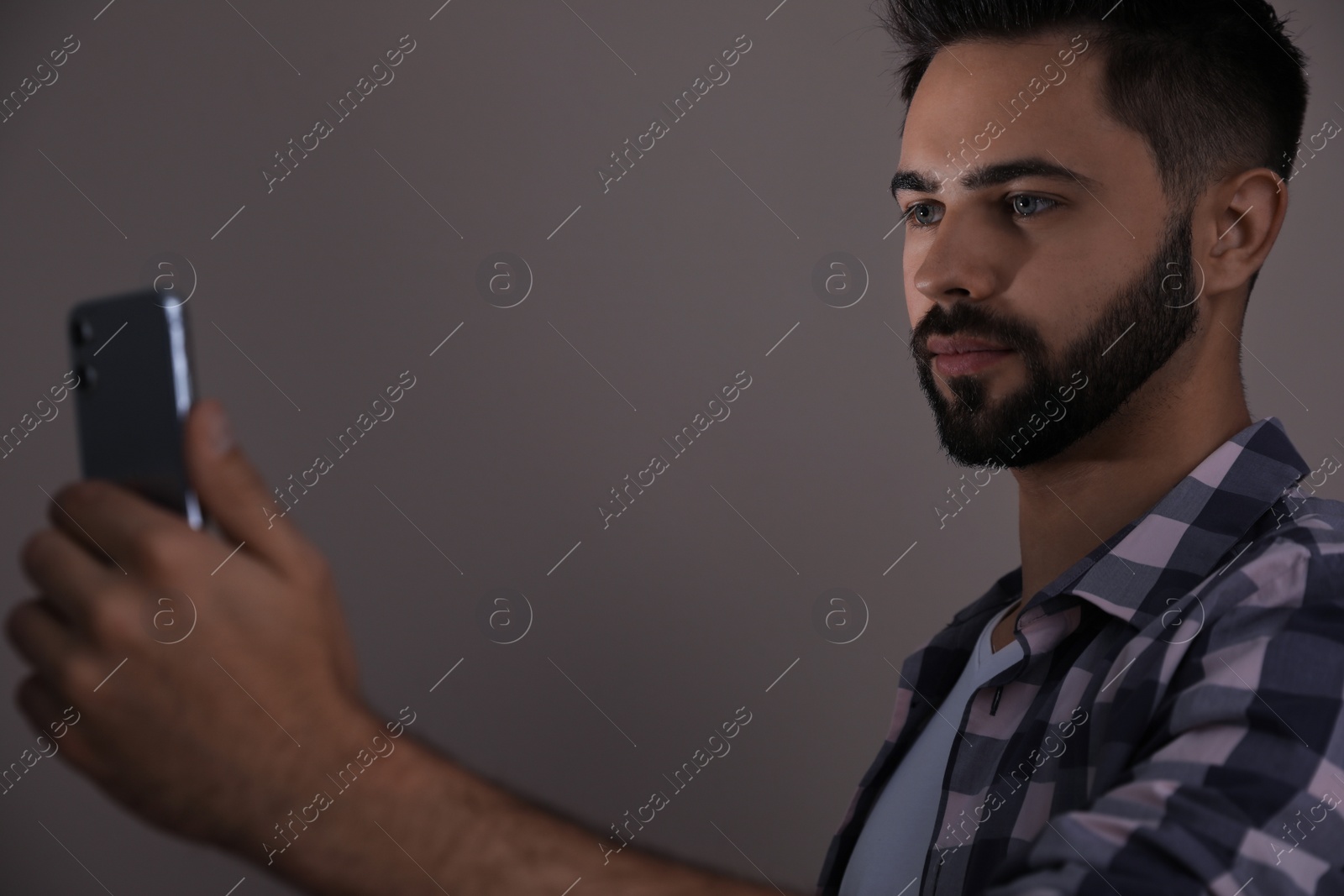 Photo of Young man unlocking smartphone with facial scanner on beige background. Biometric verification