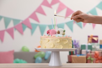 Photo of Woman lighting candle on delicious cake decorated with macarons and marshmallows in festive room, closeup. Space for text