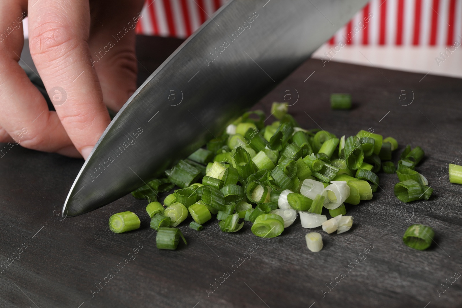 Photo of Woman cutting green spring onion on black wooden board, closeup