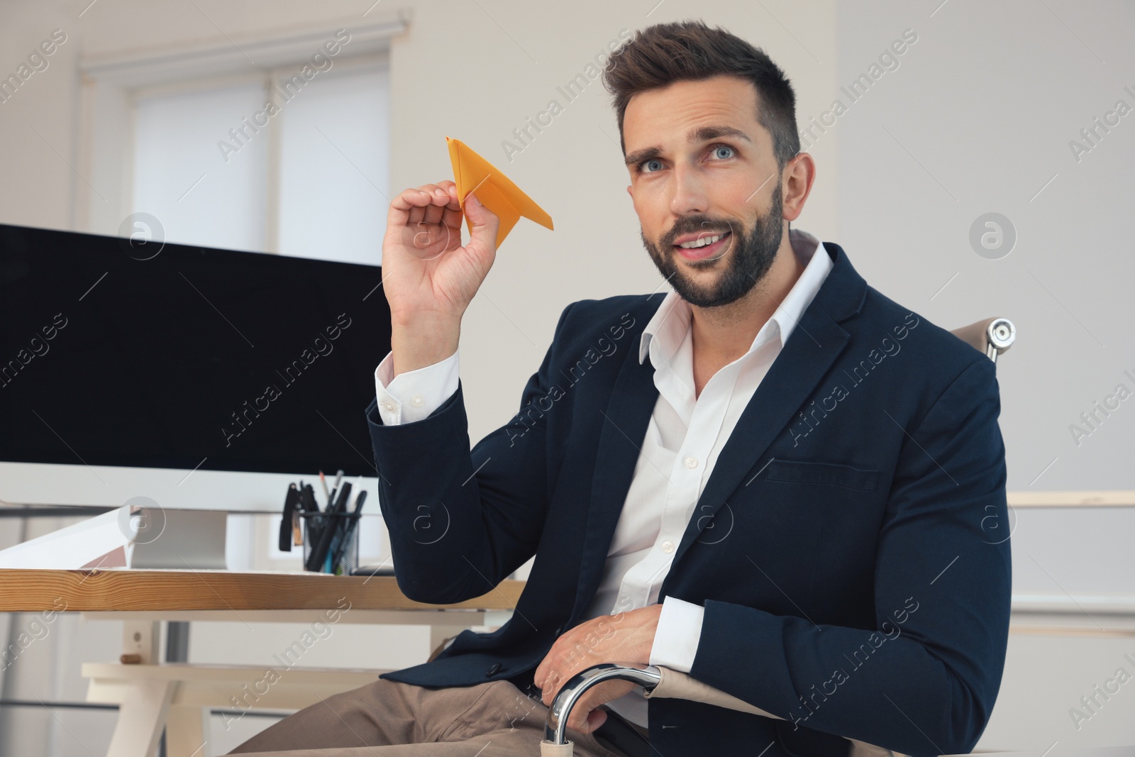 Photo of Handsome businessman playing with paper plane at desk in office