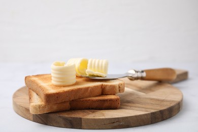 Photo of Tasty butter curls, knife and toasts on white table, closeup