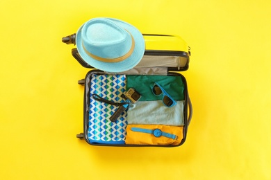 Photo of Open suitcase with summer clothes and accessories on color background, top view