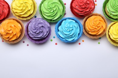 Photo of Many tasty cupcakes with bright cream and sprinkles on white background, flat lay. Space for text