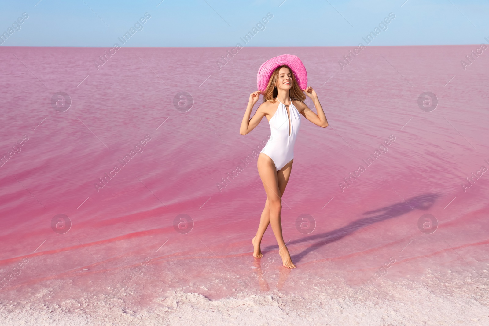 Photo of Beautiful woman in swimsuit posing near pink lake on sunny day