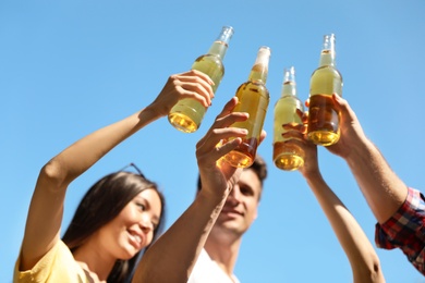 Photo of Young people holding bottles of beer against blue sky, focus on hands