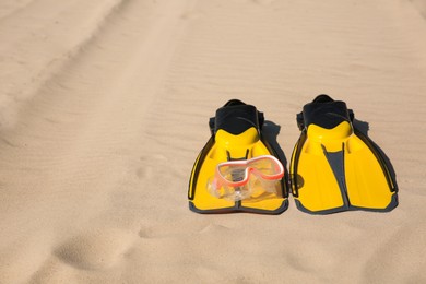Pair of flippers and diving mask on sandy beach, space for text