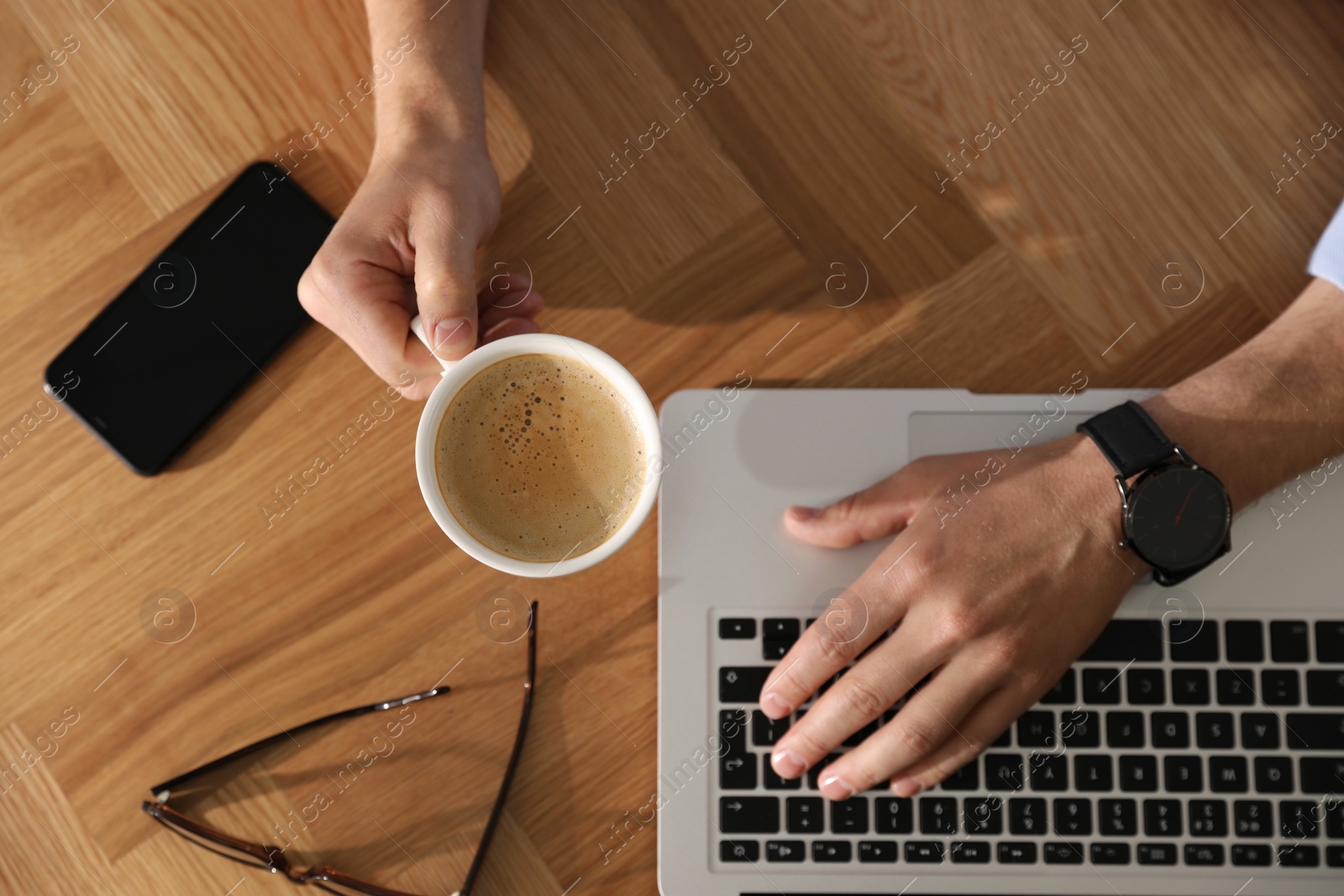Photo of Man with laptop, cup of coffee and smartphone at wooden table, top view
