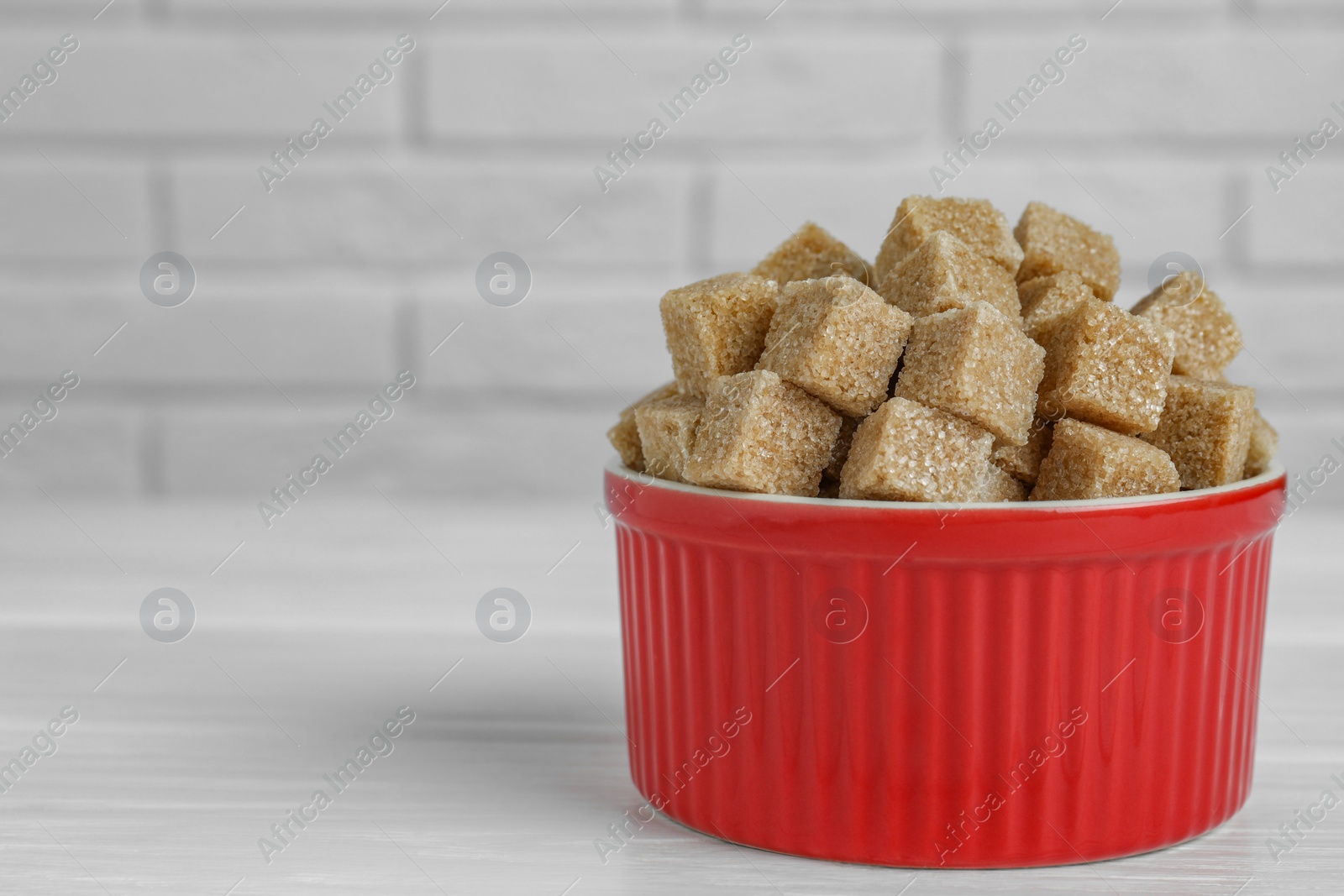 Photo of Brown sugar cubes in bowl on white wooden table, closeup. Space for text