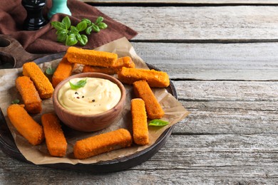 Photo of Delicious chicken nuggets and cheese sauce with basil on wooden table, space for text