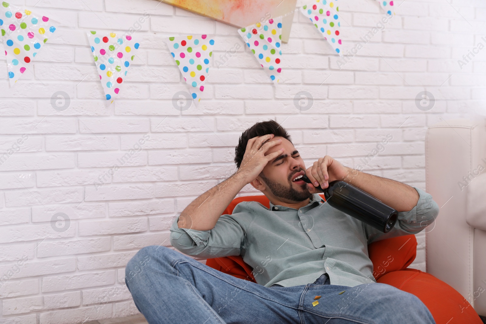 Photo of Young man suffering from hangover in messy room after party