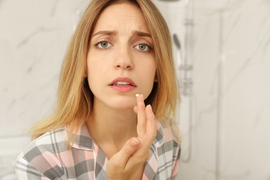 Woman with herpes applying cream onto lip in bathroom