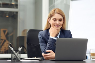 Woman working on laptop at black desk in office. Space for text