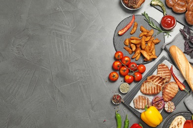 Flat lay composition with barbecued meat and vegetables on grey table. Space for text