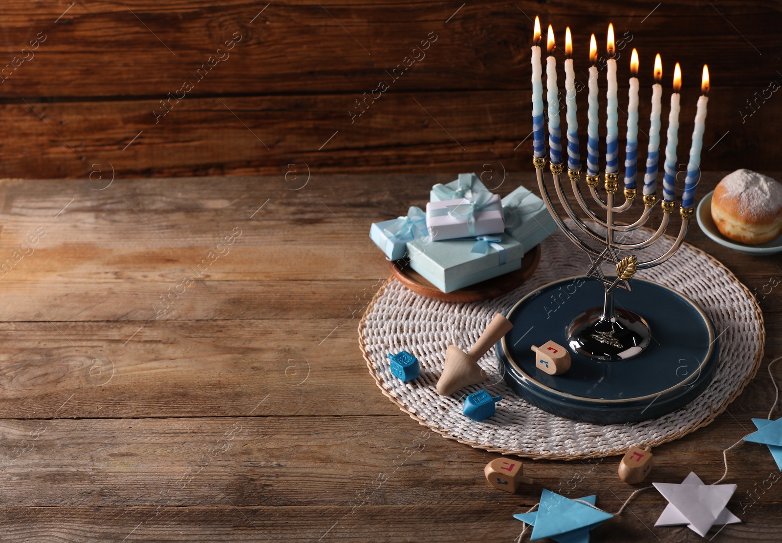 Photo of Hanukkah celebration. Menorah with burning candles, dreidels gift boxes and donut on wooden table, space for text