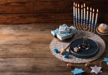 Photo of Hanukkah celebration. Menorah with burning candles, dreidels gift boxes and donut on wooden table, space for text