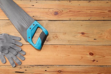 Photo of Saw with light blue handle and gloves on wooden background, flat lay. Space for text