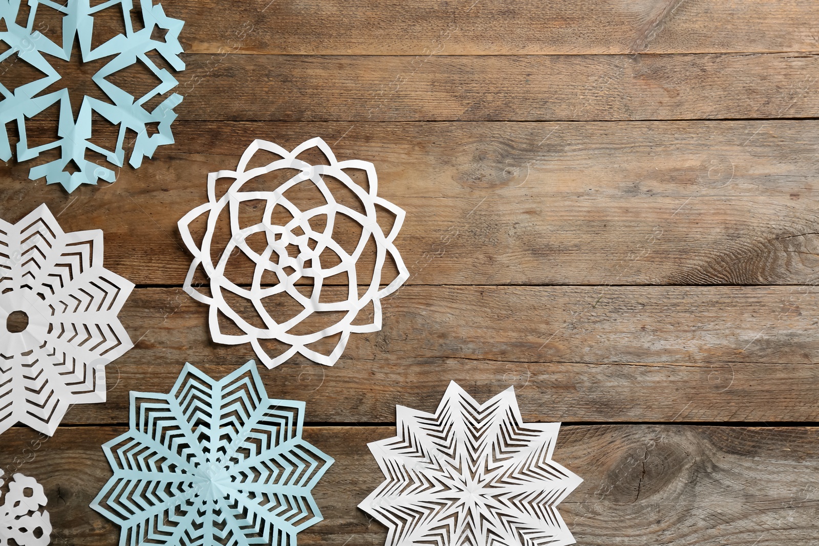 Photo of Many paper snowflakes on wooden background, flat lay. Space for text